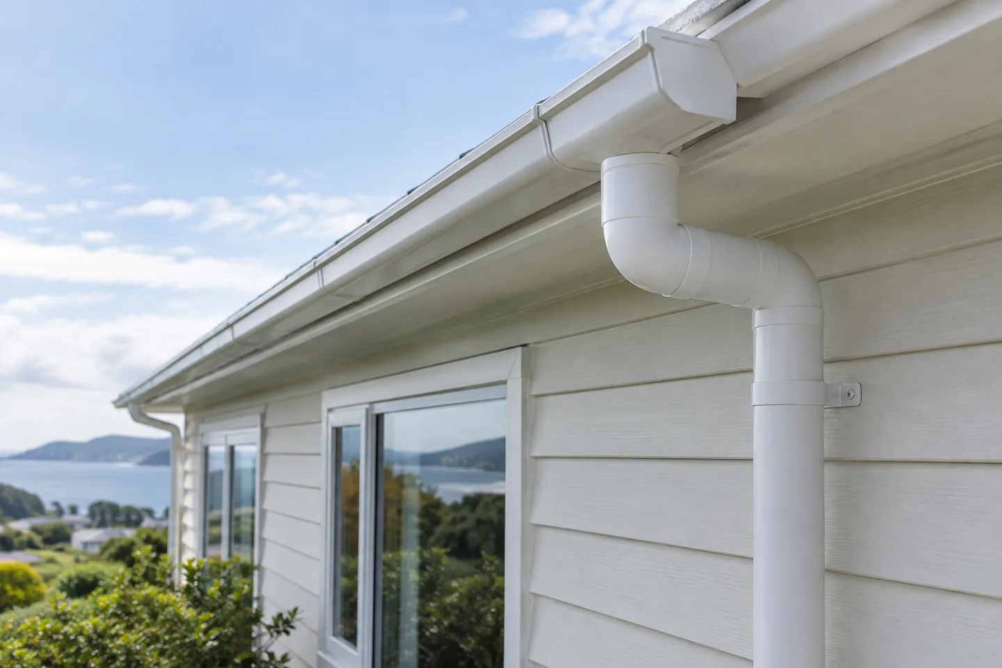 Roofing concept: White gutter and downpipe on a weatherboard home